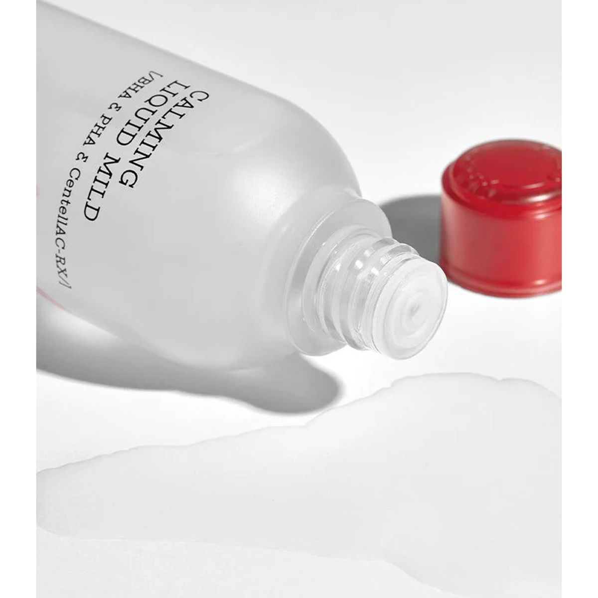 A bottle of cleansing solution next to a red cap, containing ingredients designed for acne prevention and skin soothing.