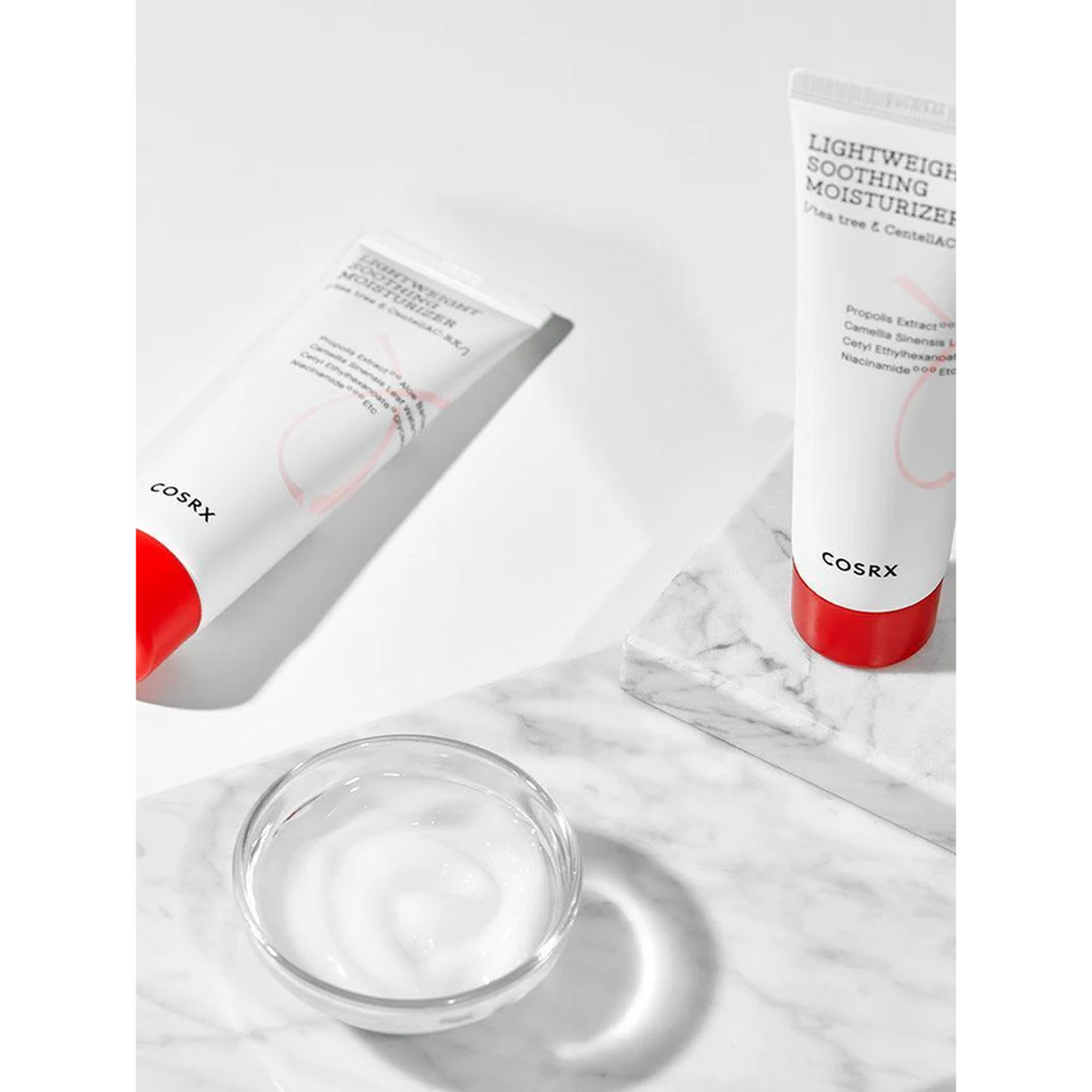 A tube of soothing moisturizer and a glass bowl on a marble surface, designed for acne-prone skin with a lightweight, non-greasy formula.